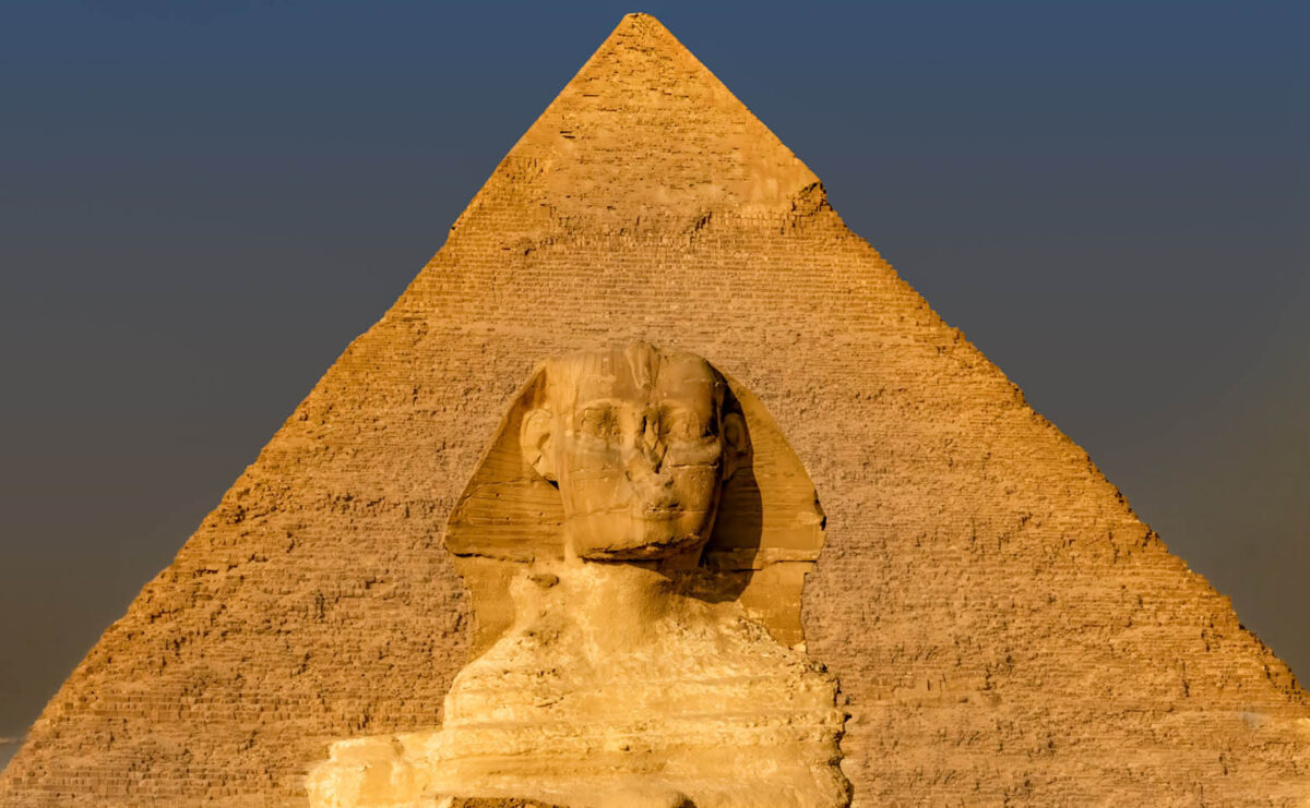 The Great Sphinx stands before the Pyramid of Khafre, its weathered face illuminated by warm light, embodying the enduring mystery of ancient Egypt.